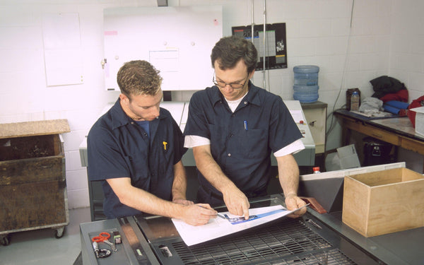 two printing operators looking at a paper on a printing press