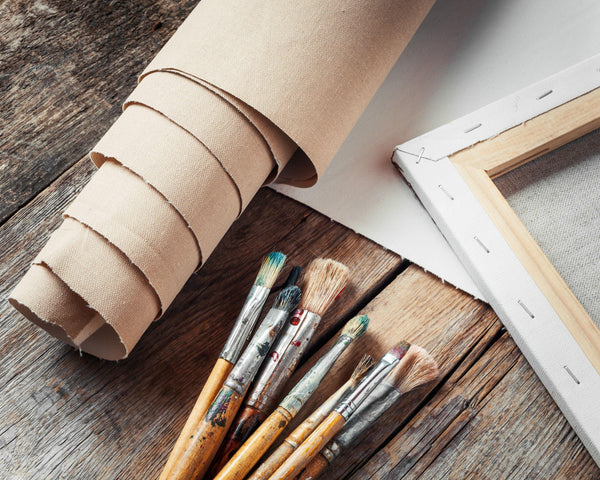 rolled canvas on a wooden floor with frames and paintbrushes beside it