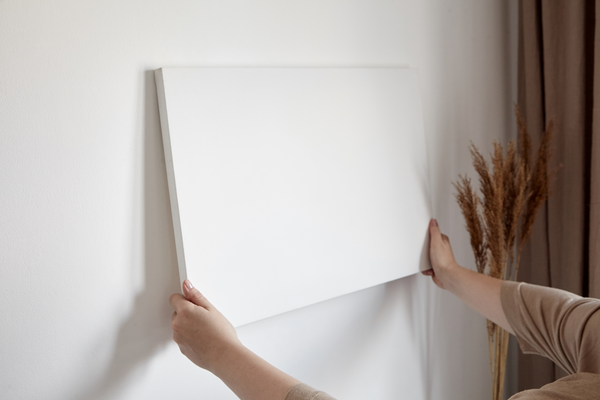 woman hanging a blank canvas on white wall